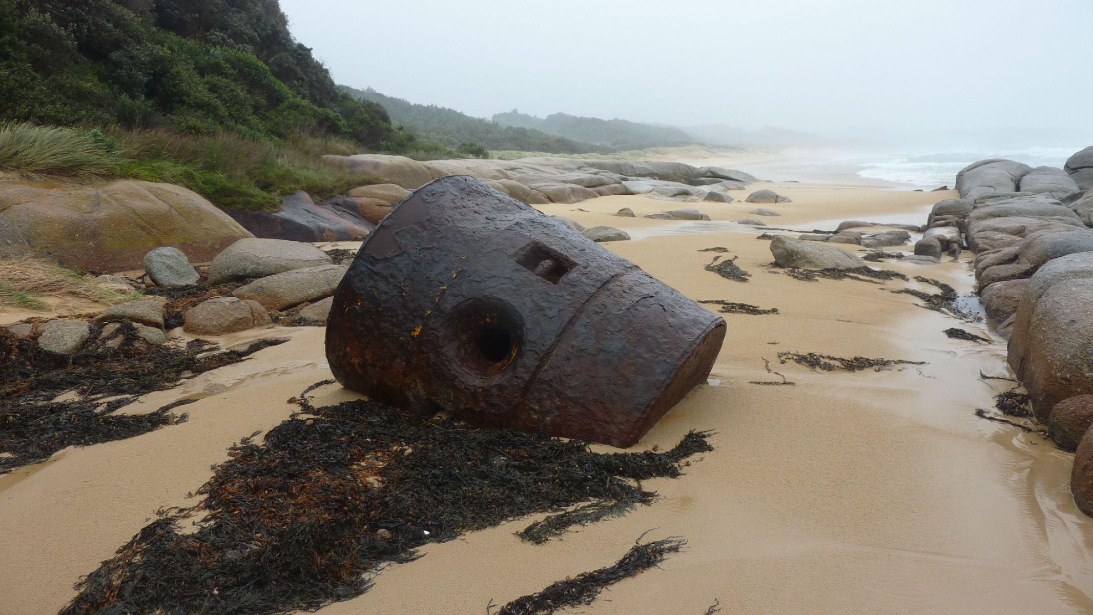 Image shows a cylindrical piece of wreckage on a beach