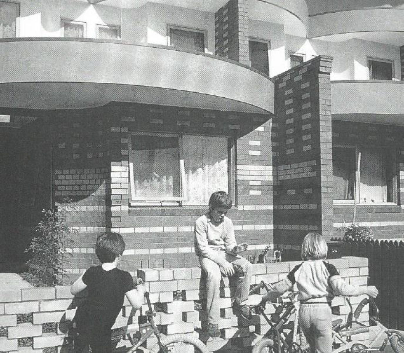 Image shows image taken at Kay Street Infill housing, Carlton. Is a black and white image with children standing out the front of the building with their bikes.