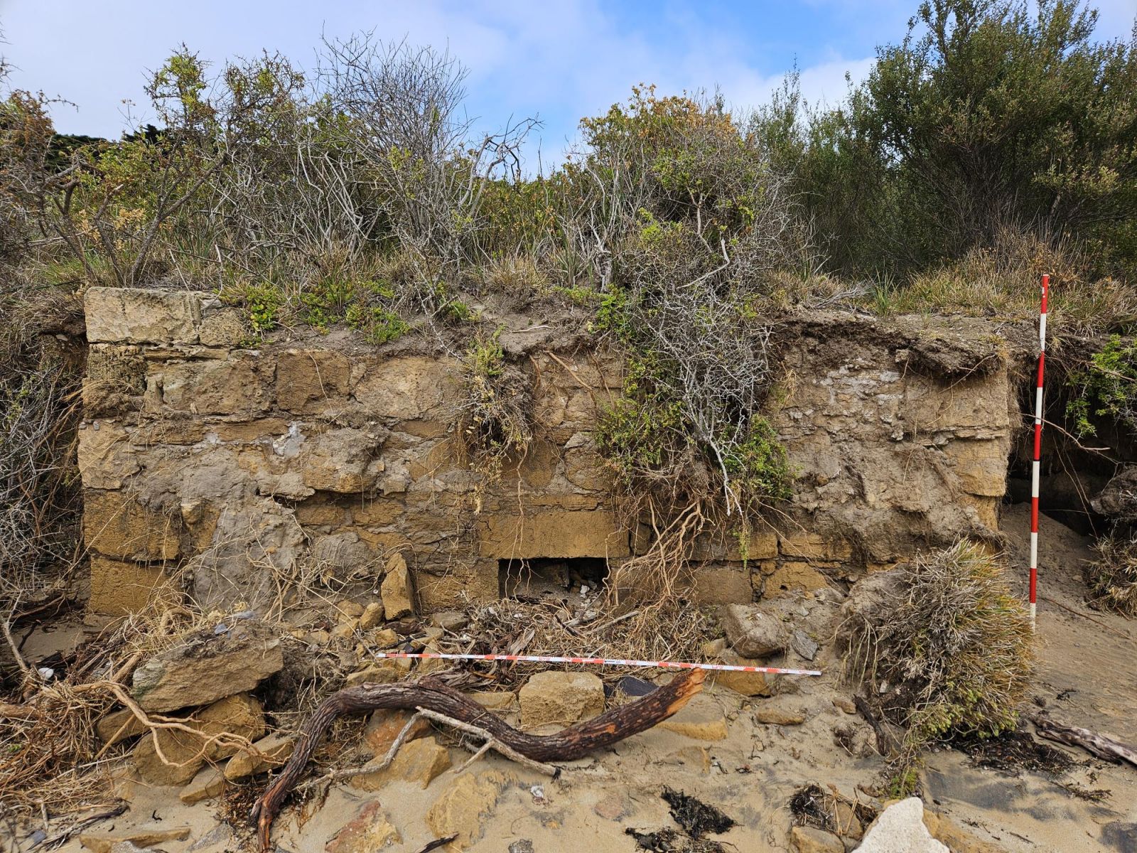 A lime kiln can be seen amongst scrubs and sandy soil.The kiln is sandstone in colour. 